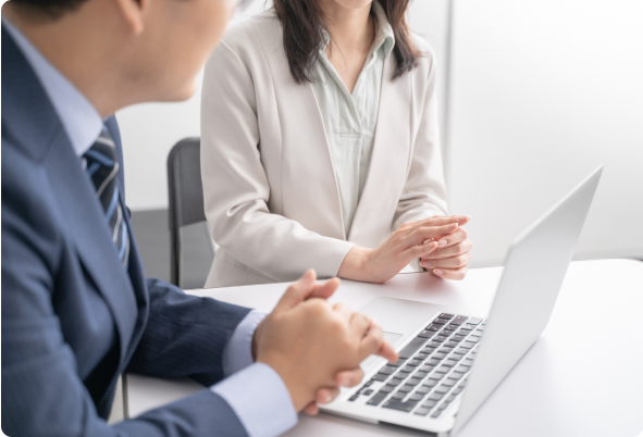 スーツを着た男性と女性がノートパソコンを前に会話している